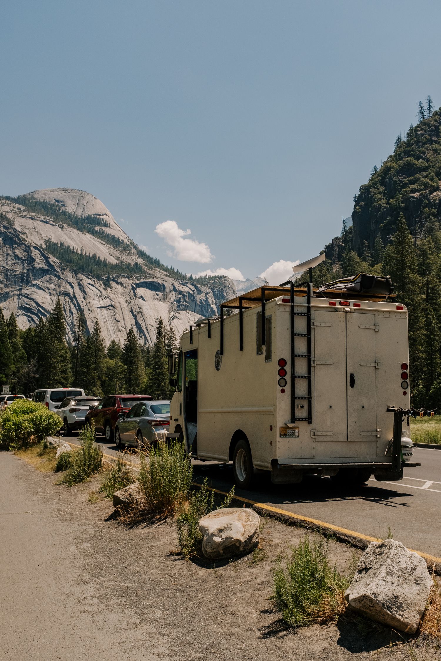 RV camper parked on mountain road with towering granite cliffs of Yosemite National Park in background.