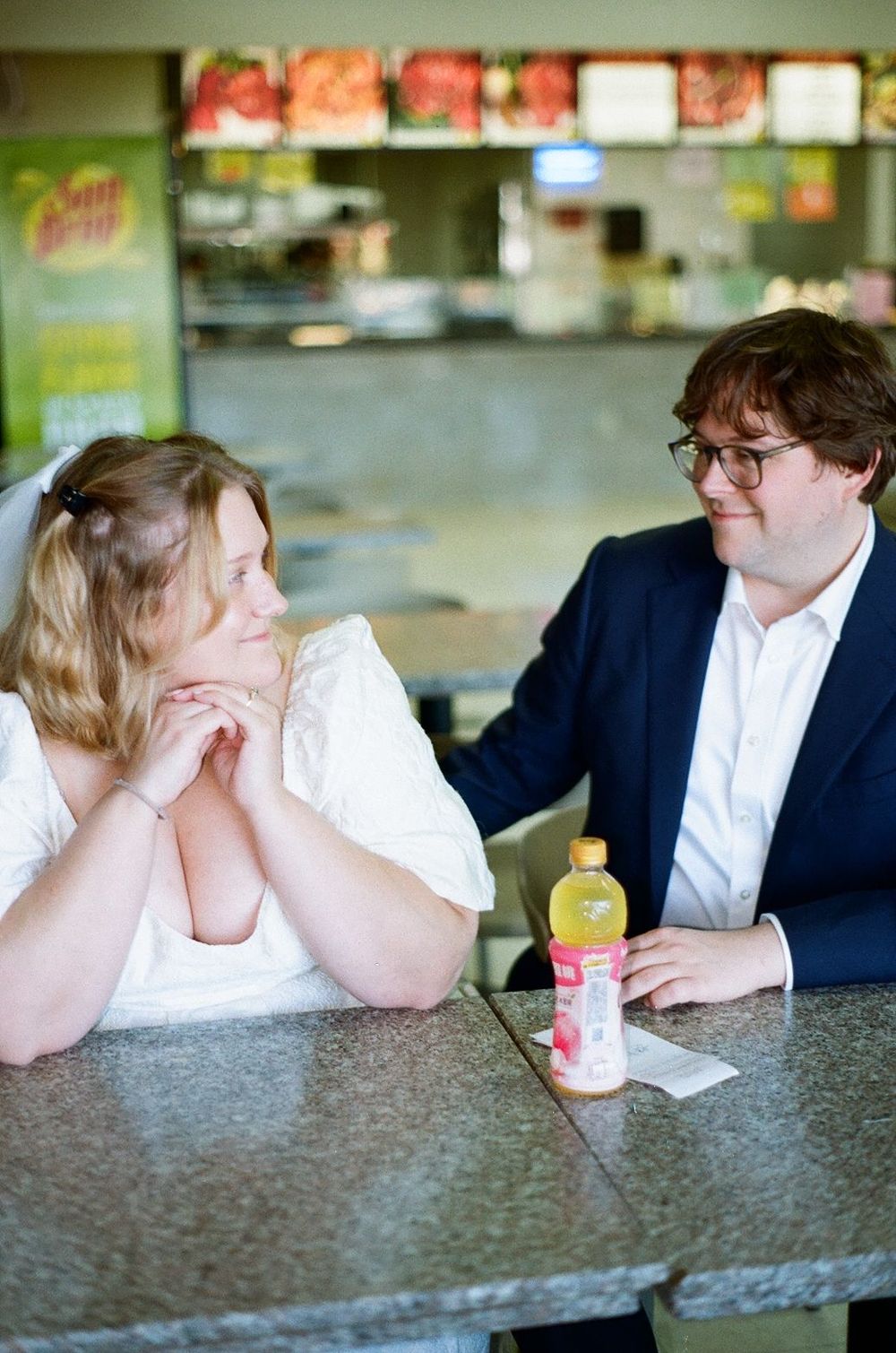 A couple sitting together at a counter in a casual restaurant with a beverage bottle on the table.