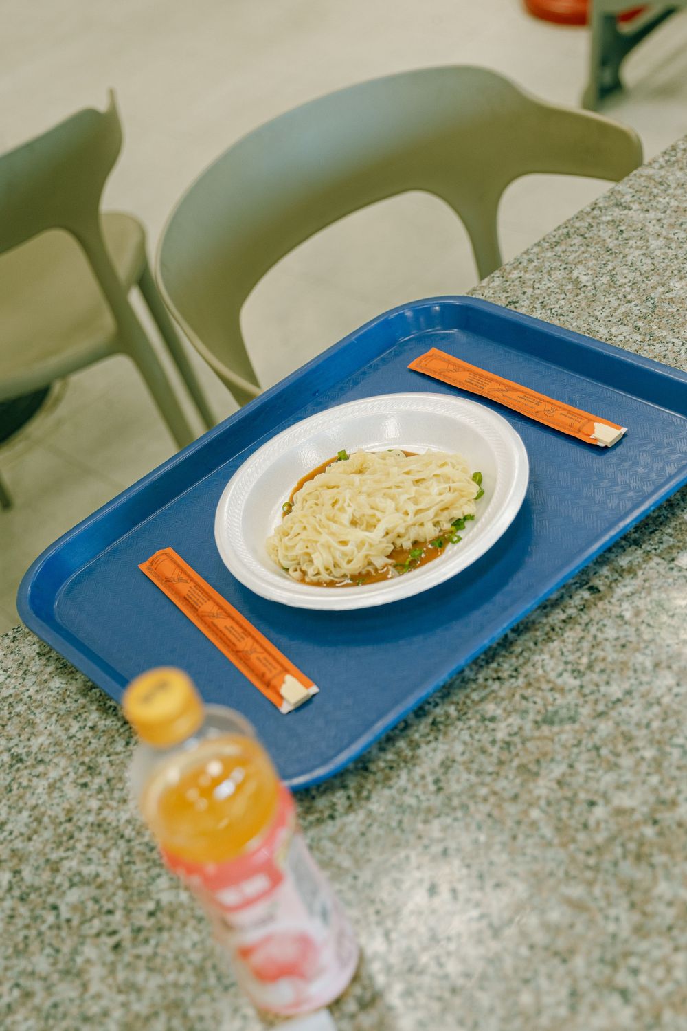 A blue cafeteria tray with rice and peas on a white plate sits next to an orange beverage bottle.