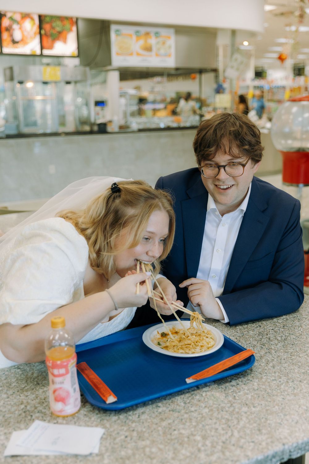 Two people share a casual meal at a fast food restaurant counter with a tray of food and pink drink.
