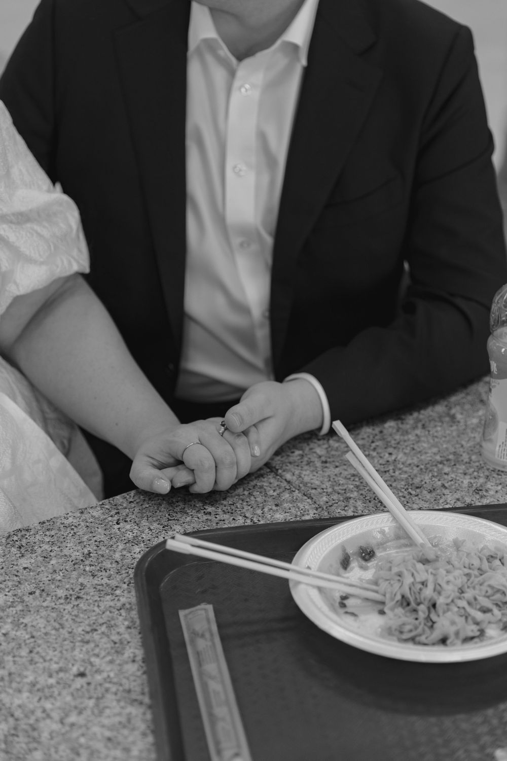 Black and white photo of two people holding hands at a table with a plate of noodles.
