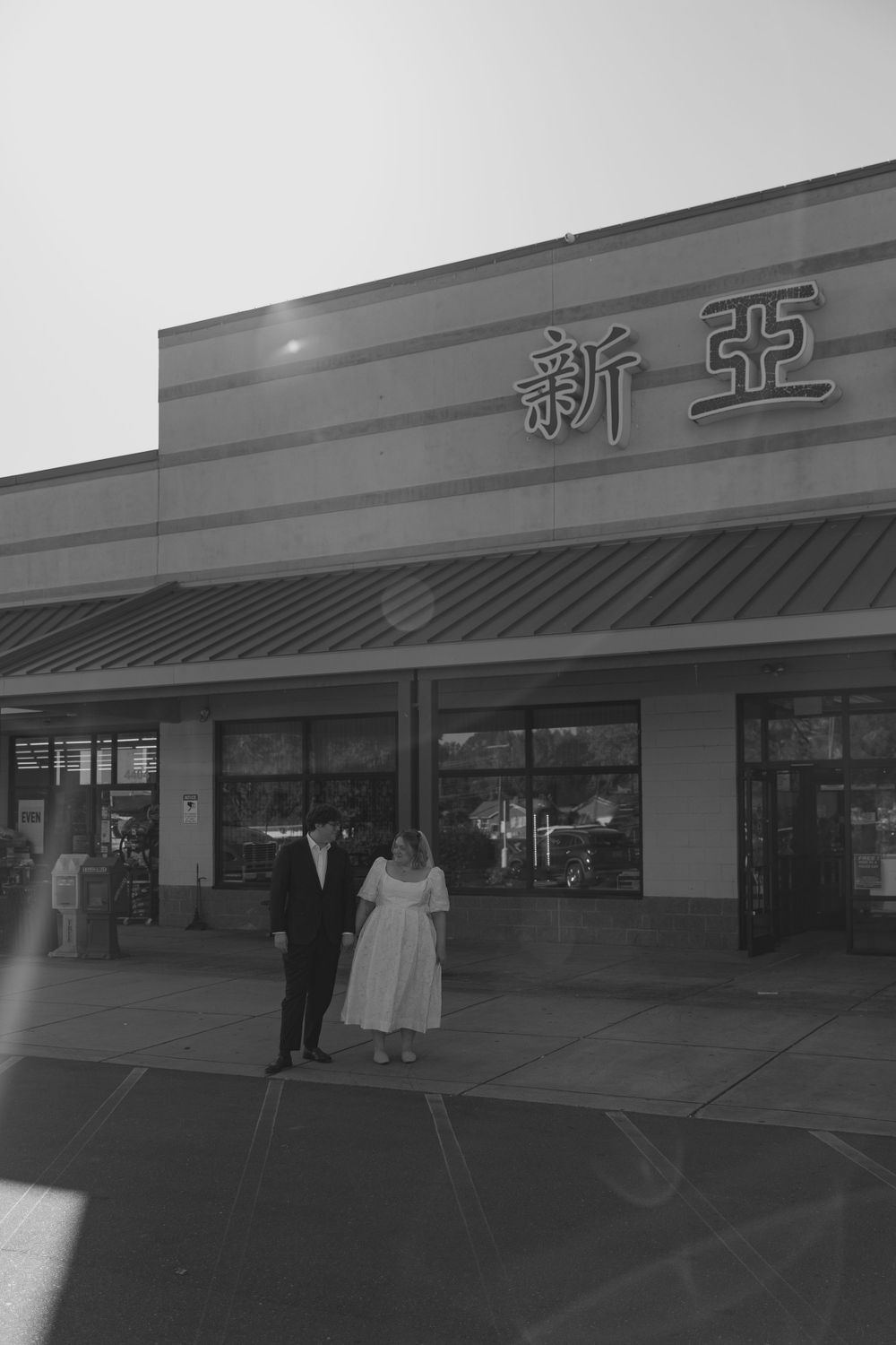 Black and white photograph of people standing in front of an Asian grocery store with Chinese characters on the storefront.