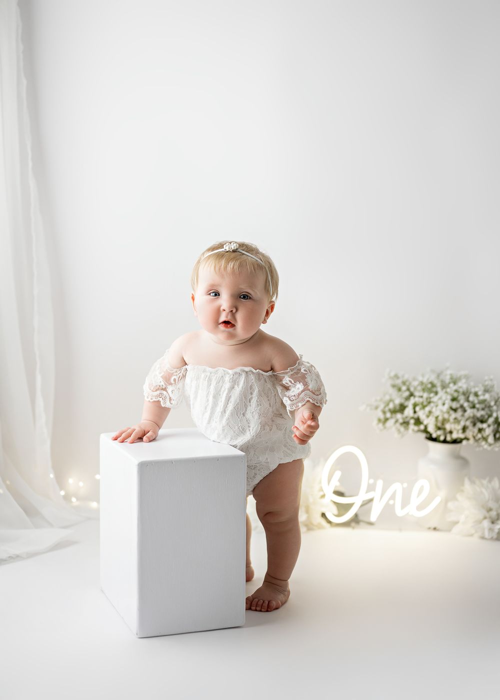 A white studio setup with minimalist decor featuring a small white pedestal and illuminated 'One' sign.