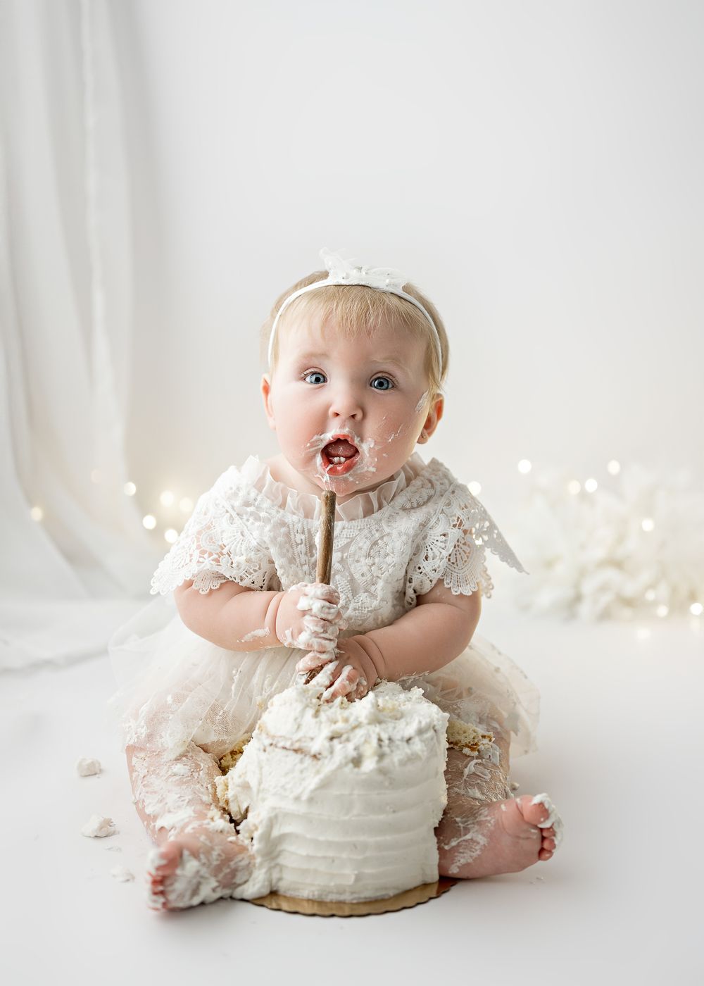 First birthday cake smash photography session with white frosted cake and lace dress.