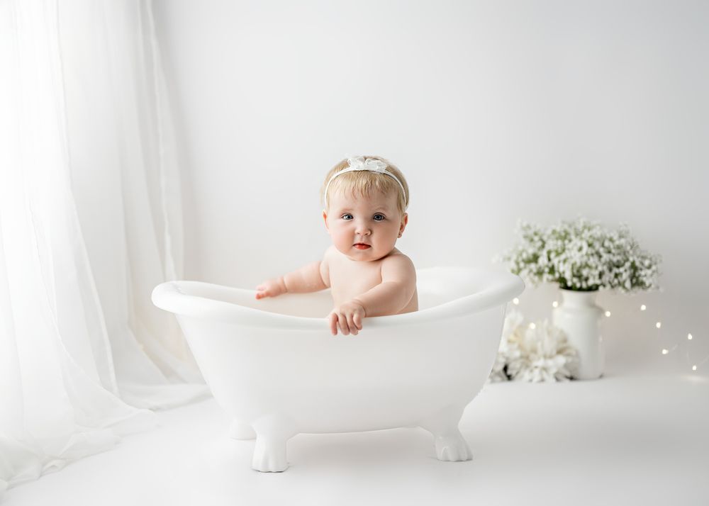 Vintage-style miniature bathtub photo setup with white florals and soft lighting.