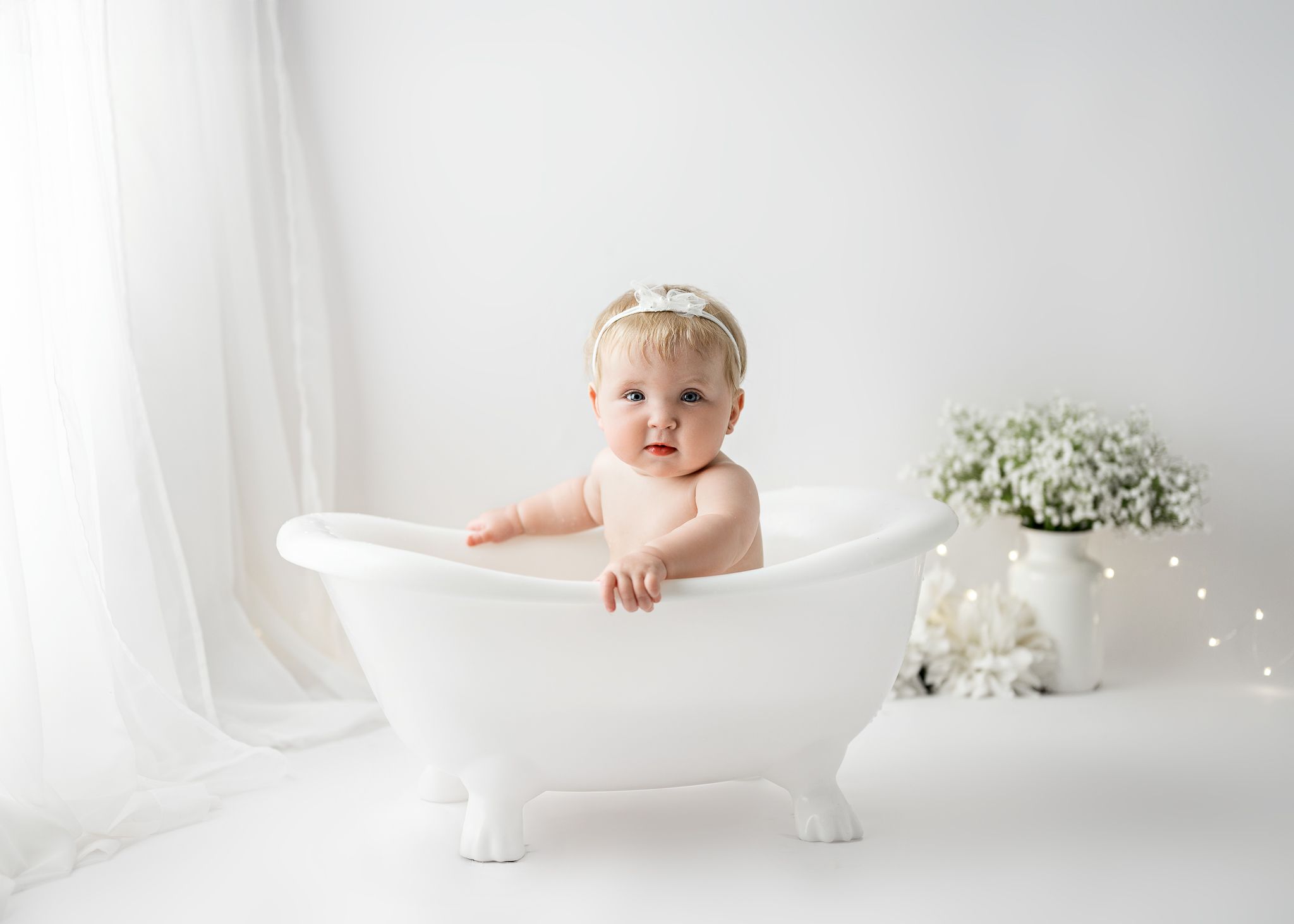 Vintage-style miniature bathtub photo setup with white florals and soft lighting.