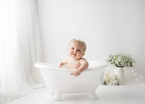 Joyful bath time photo session in antique white tub with baby's breath flowers and twinkle lights.