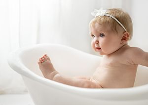 Baby playing in white freestanding bathtub with natural window light and white backdrop.