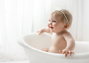 Baby smiling while peeking over edge of white vintage bathtub during photo session.