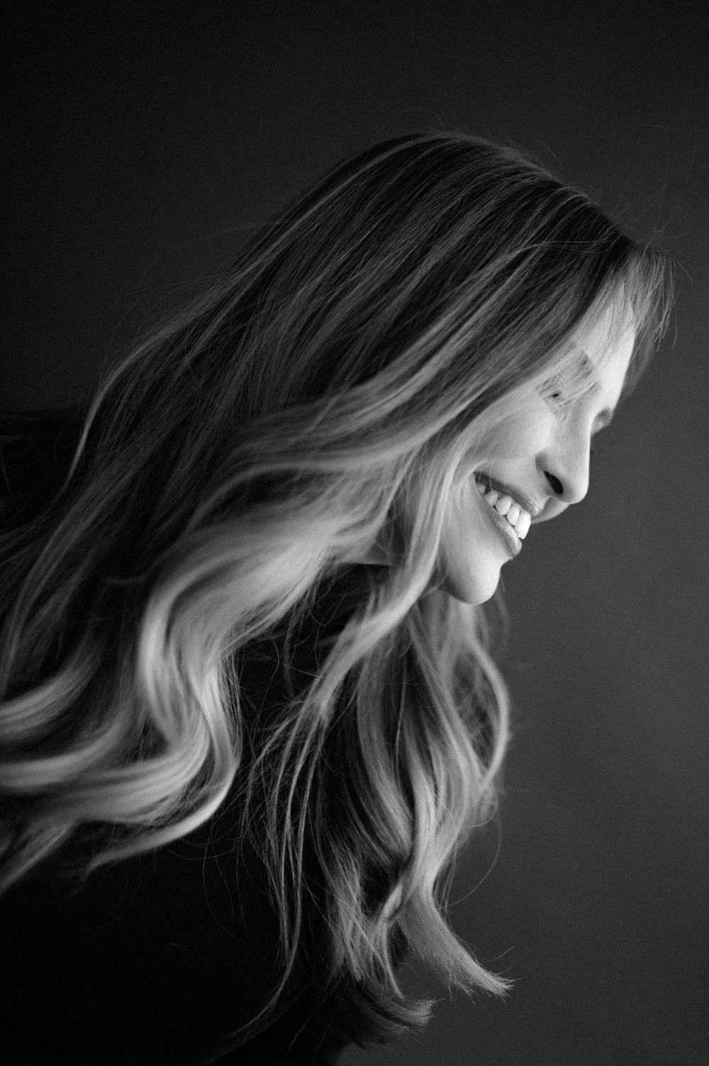 Candid black and white profile shot capturing a genuine laugh and flowing hair.