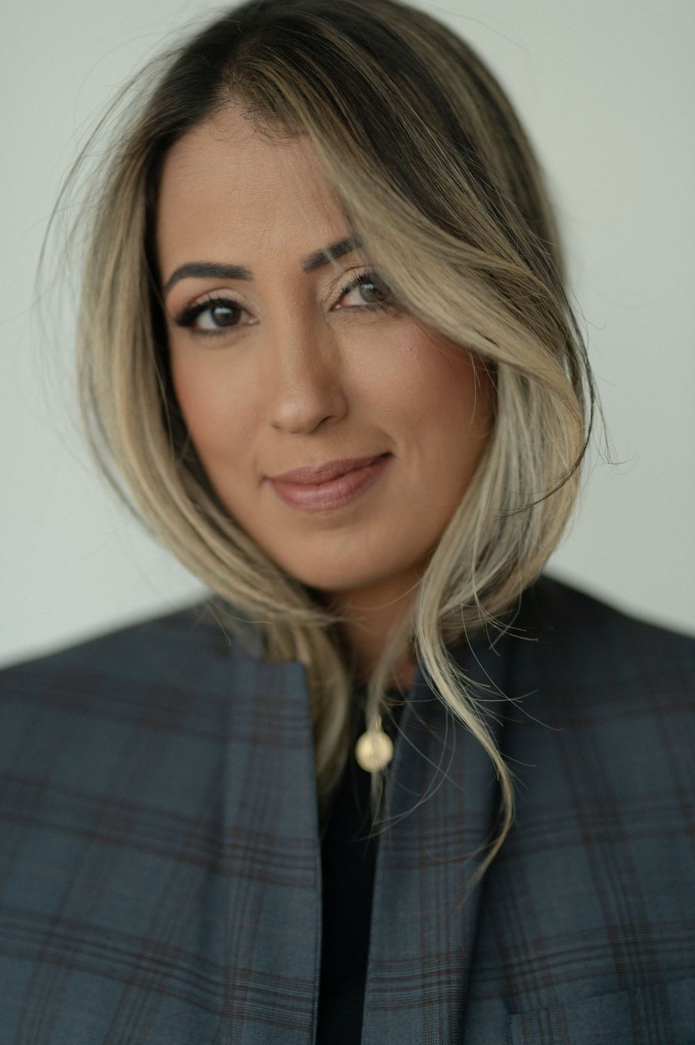 Professional portrait featuring blonde highlights and a plaid blazer against a light background.