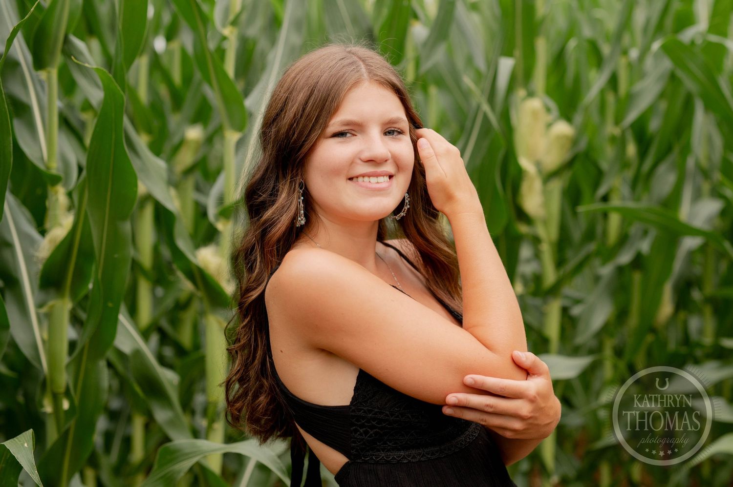 Portrait of woman in black top posing against green cornfield backdrop.