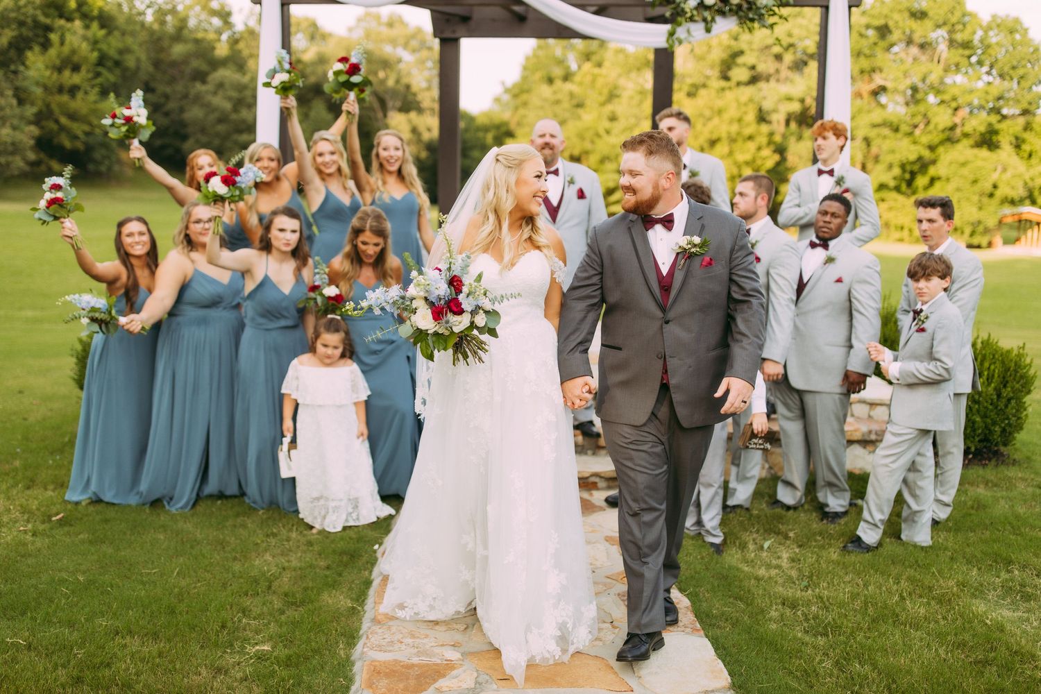Wedding party celebrates with joy on a sunny day at an outdoor garden ceremony.
