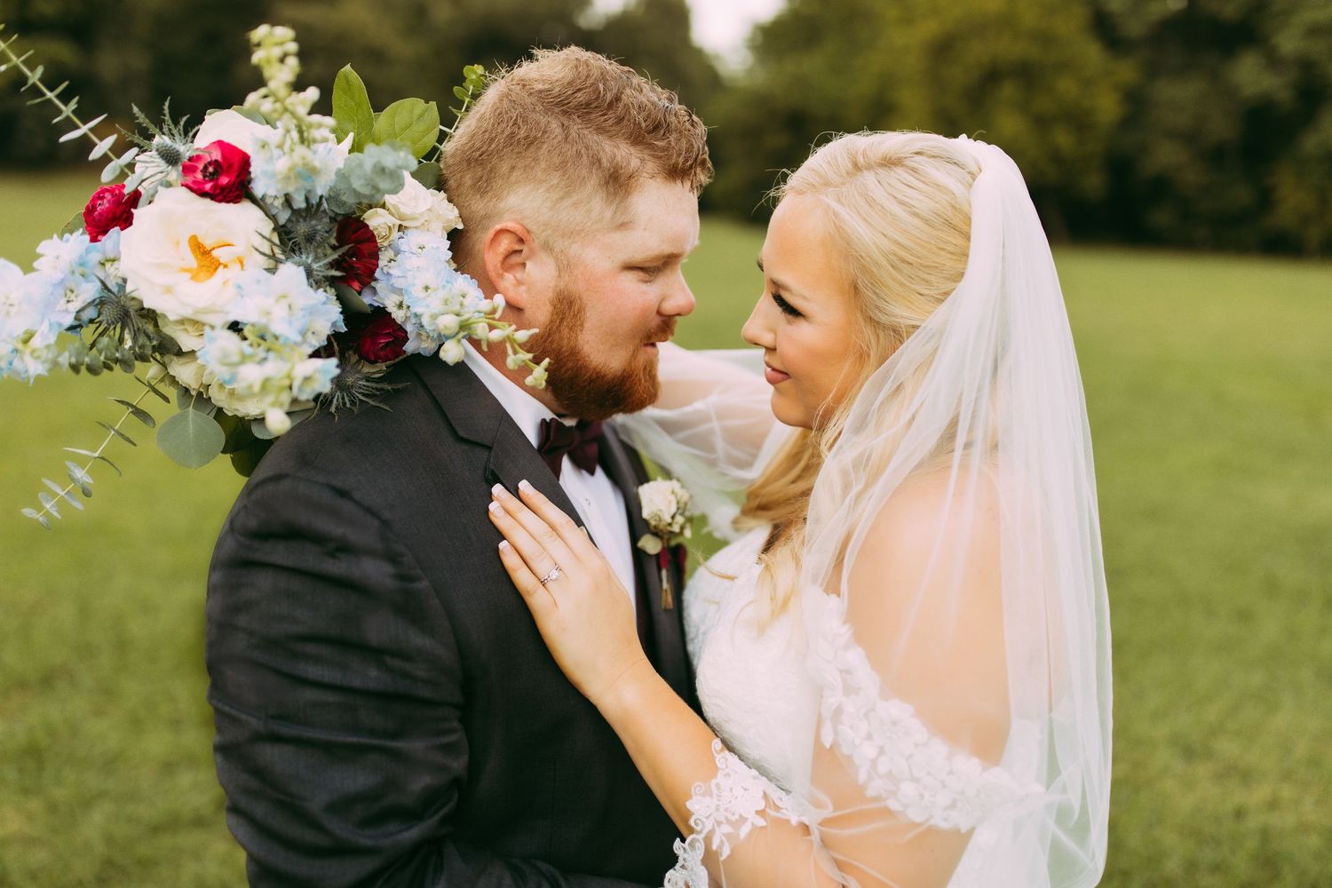 A joyful couple shares a romantic moment on their wedding day in a lush green field with a beautiful floral bouquet.