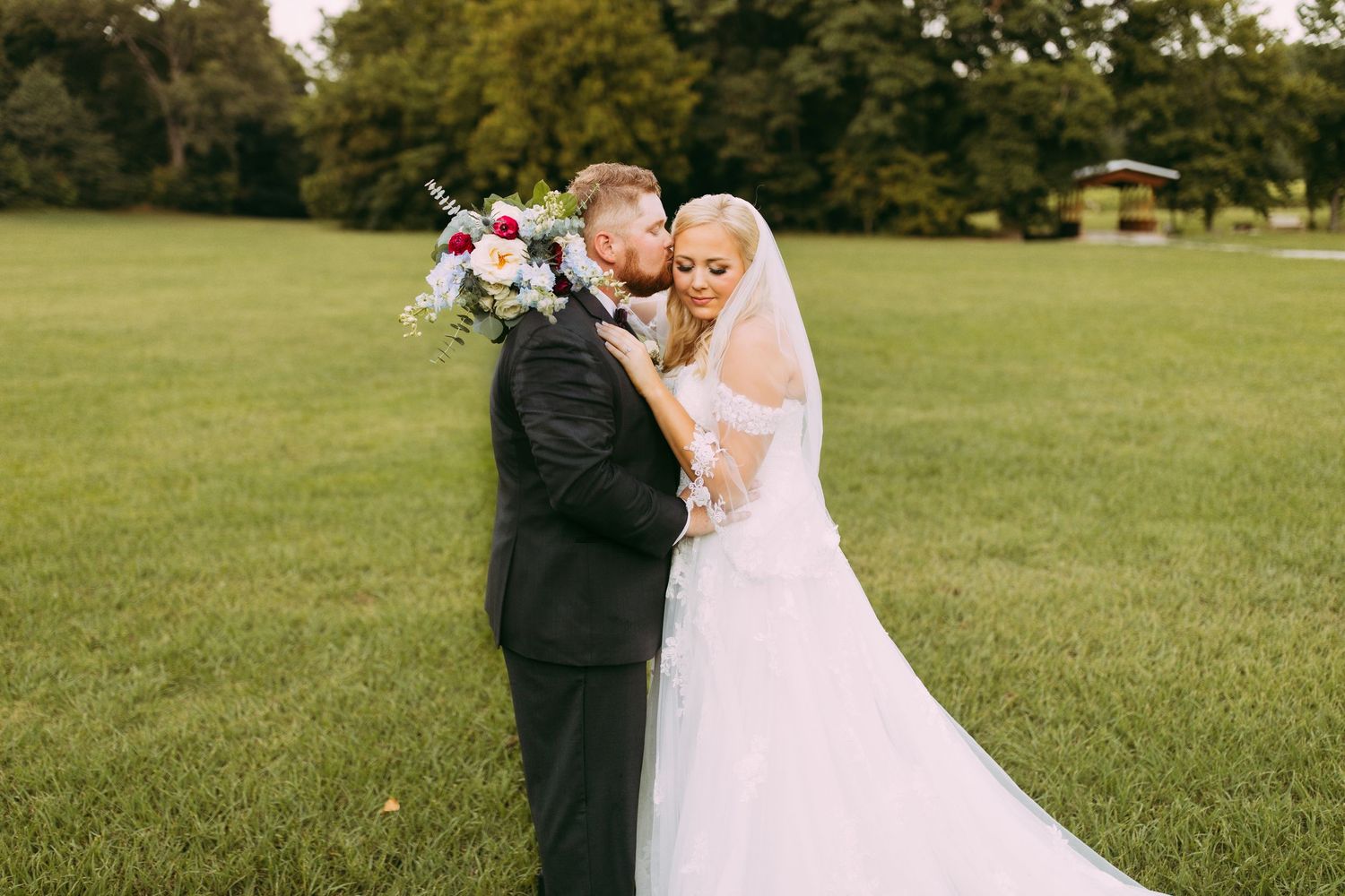 A couple shares a romantic moment on their wedding day in a lush green field.
