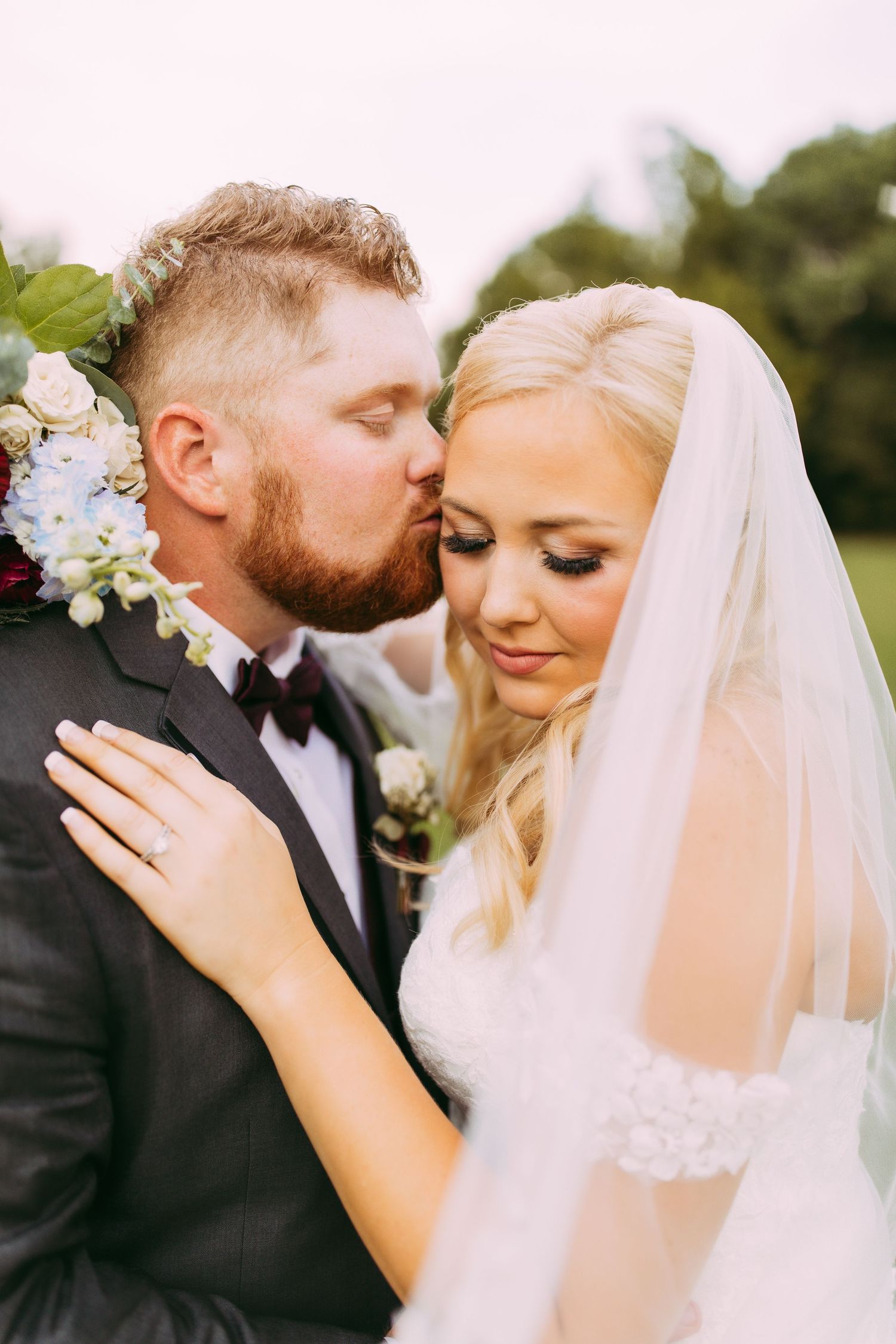 A romantic wedding portrait featuring a tender moment between newlyweds outdoors with floral bouquet details.