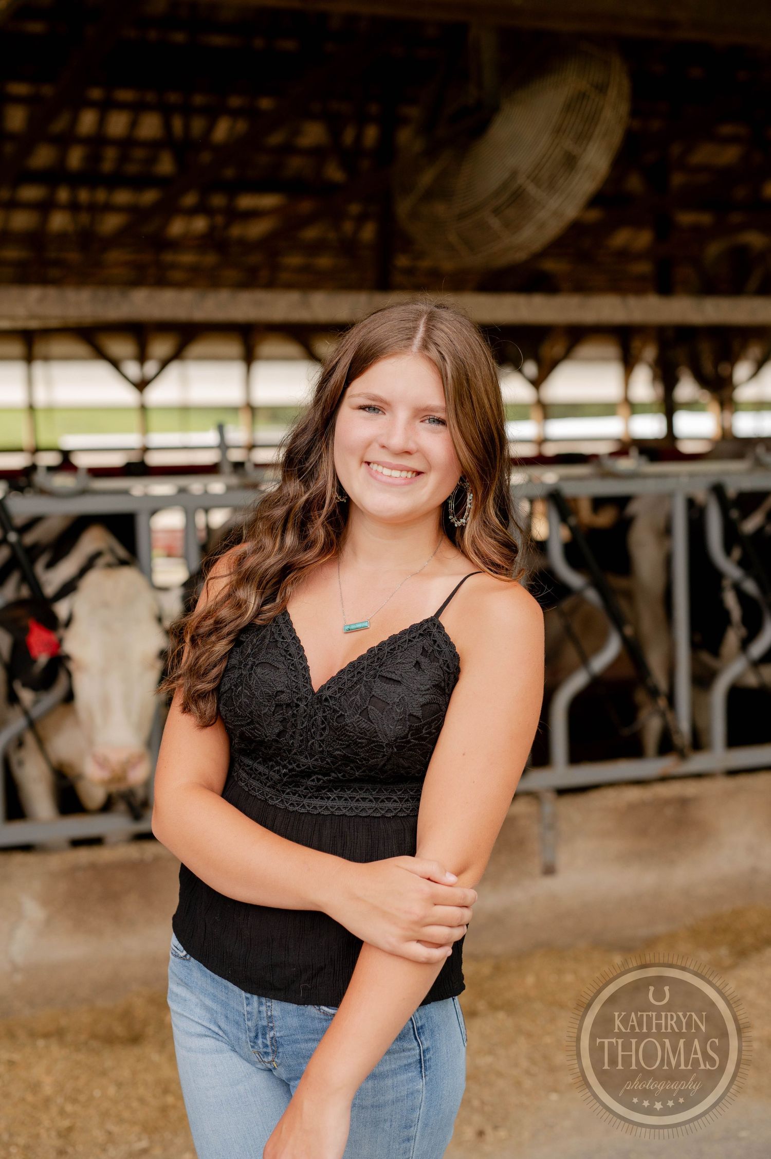 Portrait in a black lace top taken inside a rustic barn with dairy cows in background.