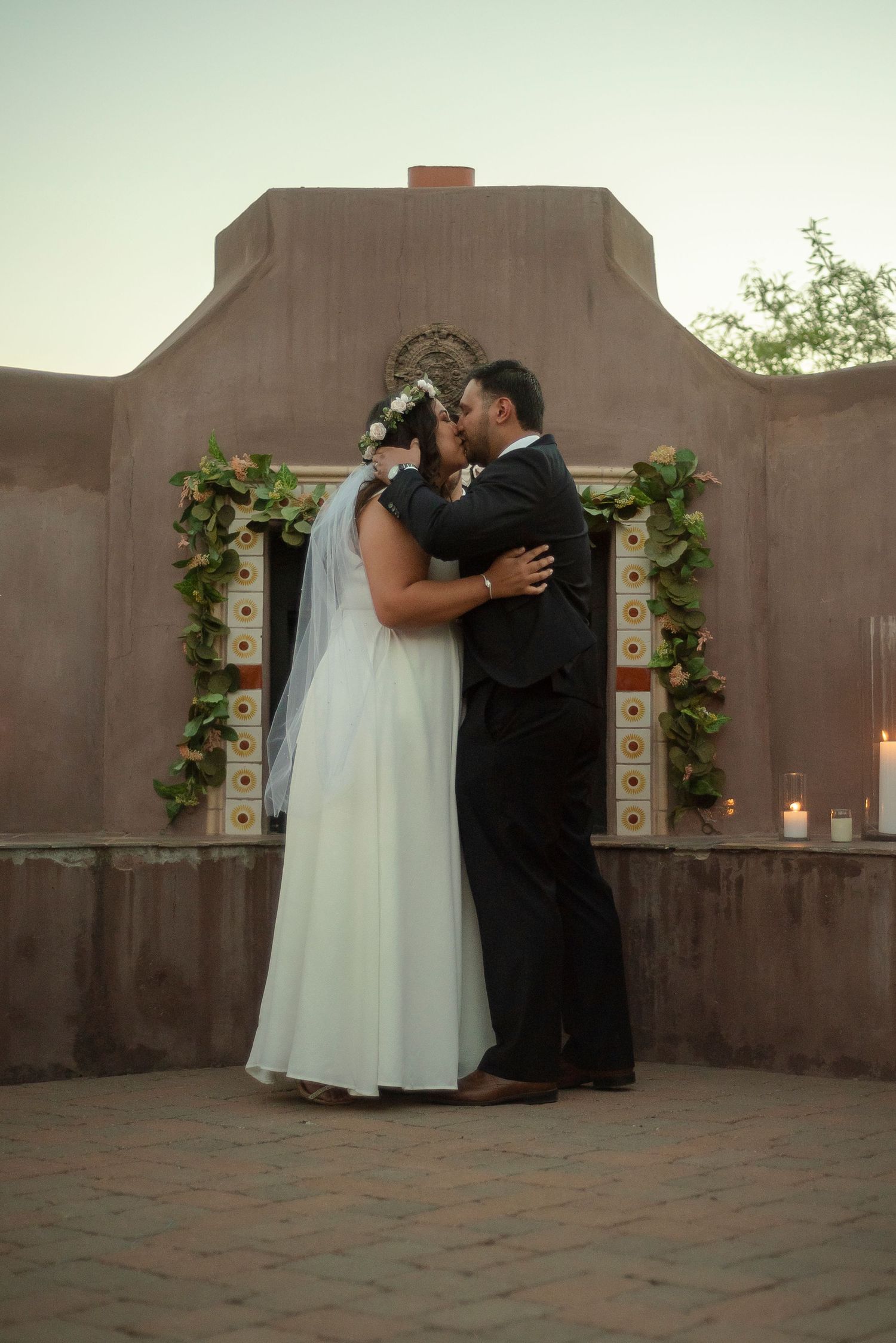 Joyful newlyweds walk down aisle at outdoor ceremony surrounded by guests in black attire on brick patio.