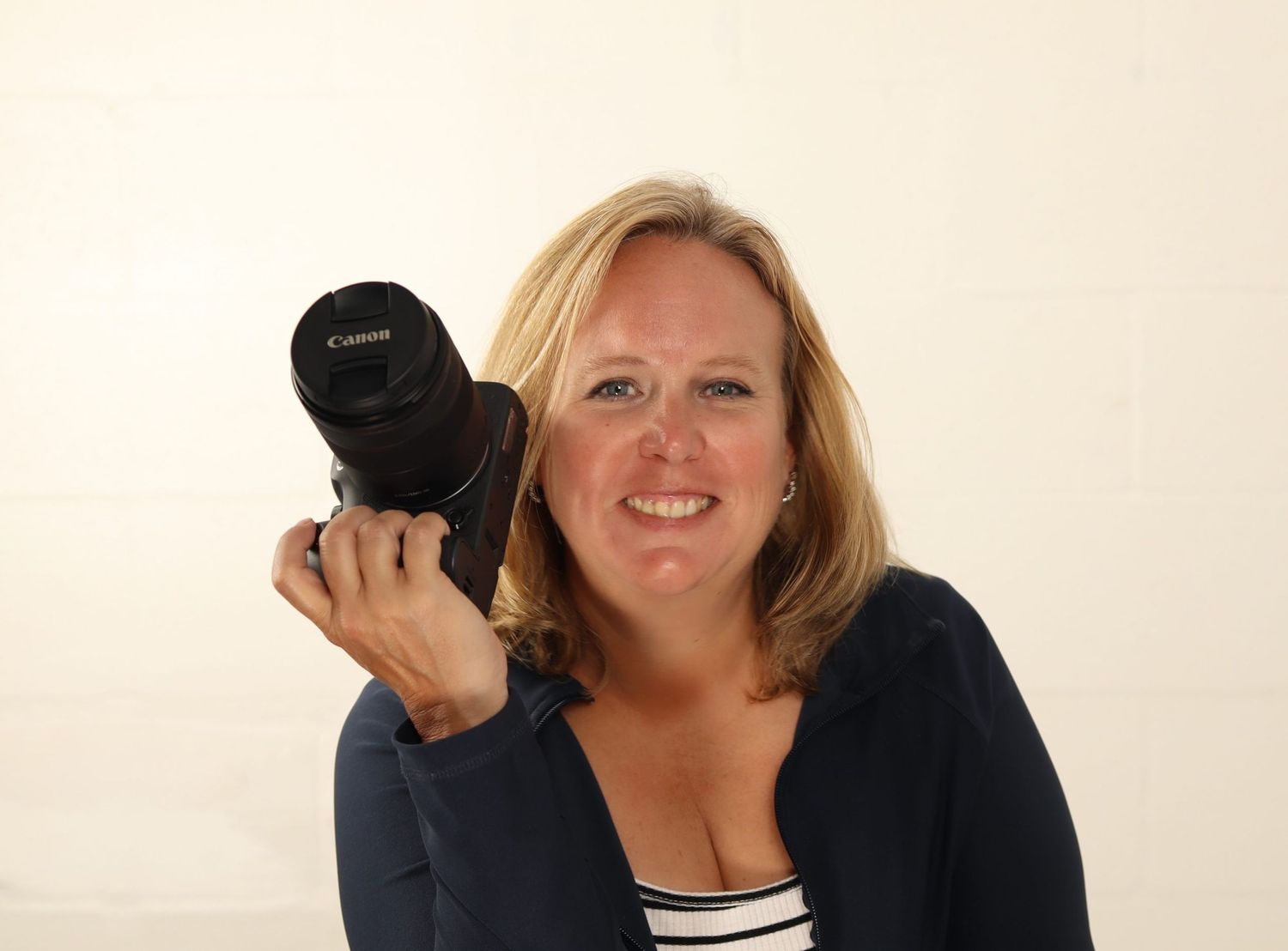 Professional photographer in a navy top holding a camera against white background.