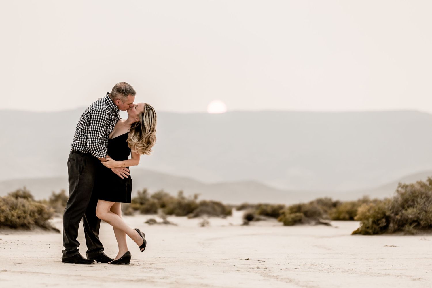A romantic couple embraces during sunset in a desert landscape with muted colors and soft lighting.