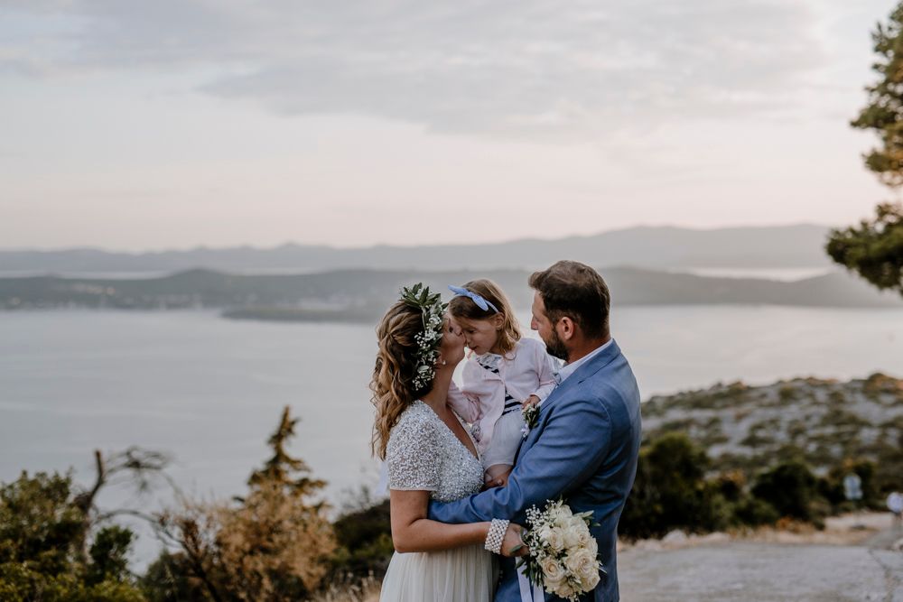 A couple and their child share an intimate moment on a hilltop overlooking a misty lake during sunset.