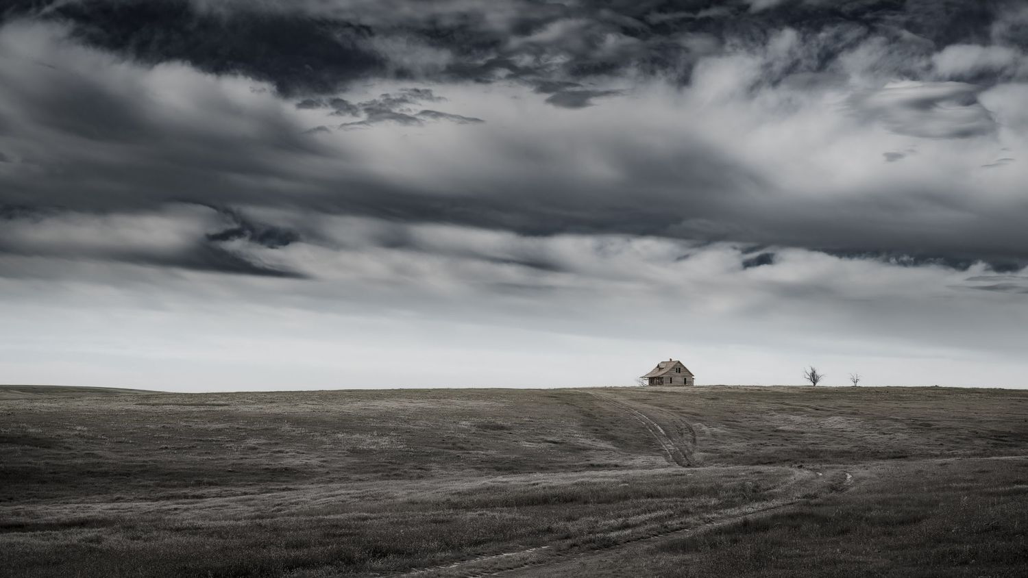 Desolate prairie landscape with distant trees under dramatic overcast skies.