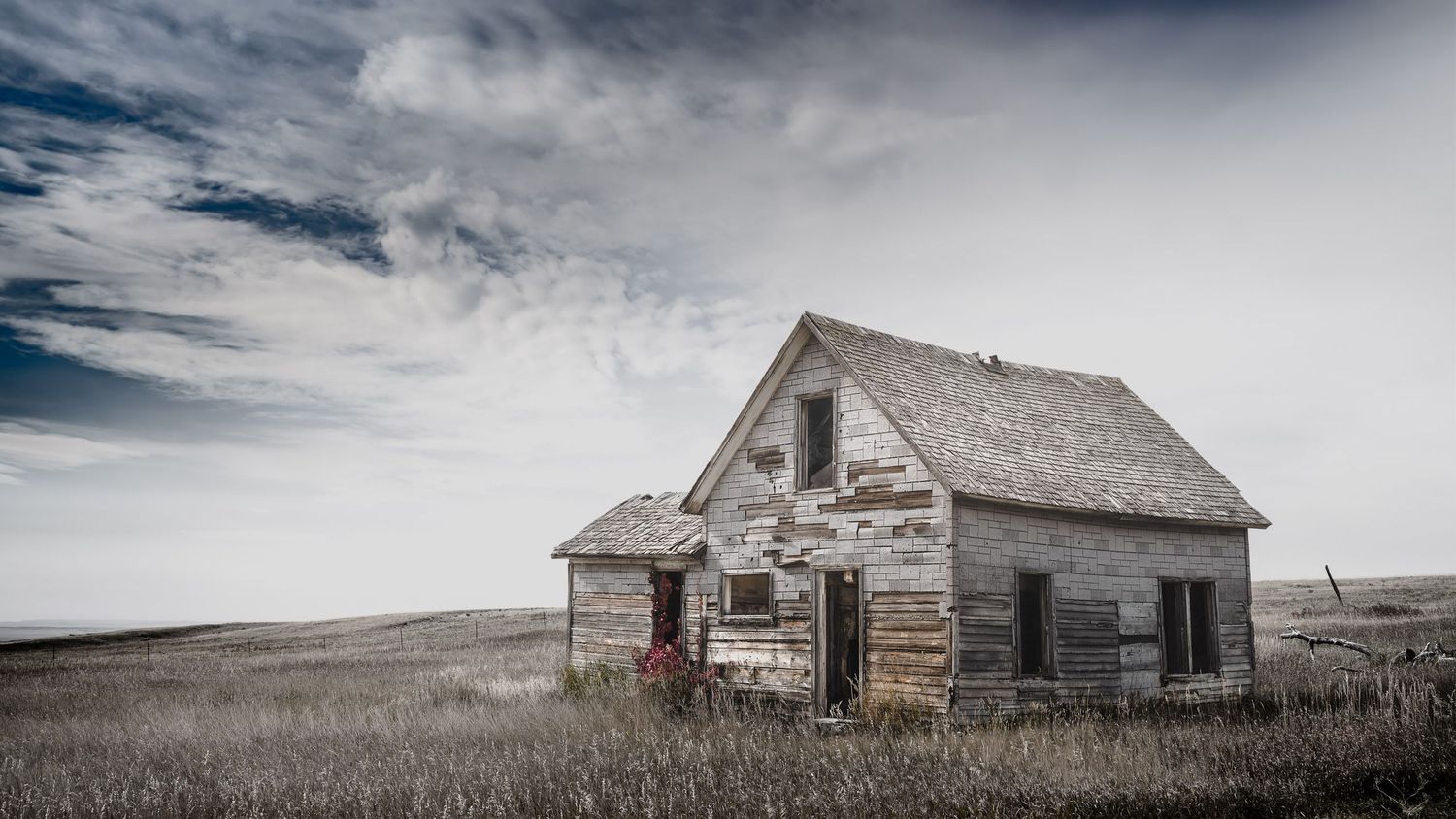 Dilapidated wooden homestead with peeling paint sits isolated on the prairie.