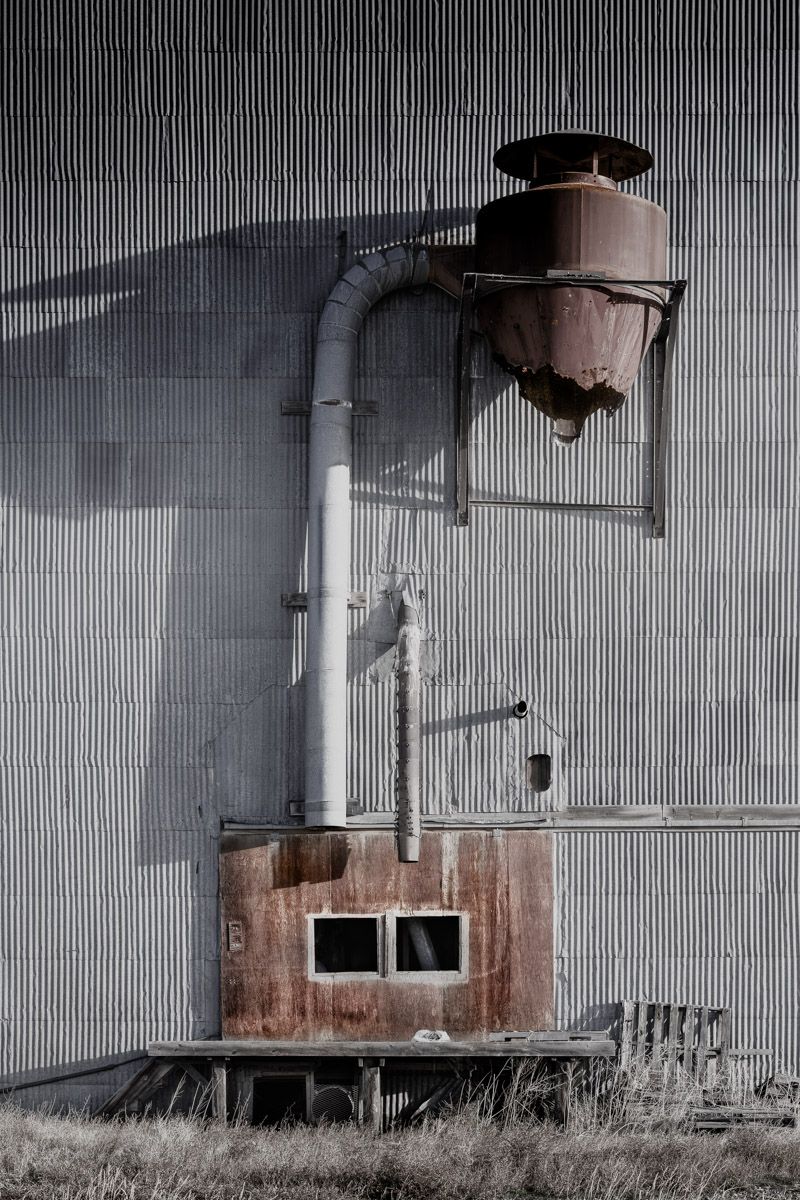 Industrial ventilation system with rusty pipes mounted on corrugated metal wall.