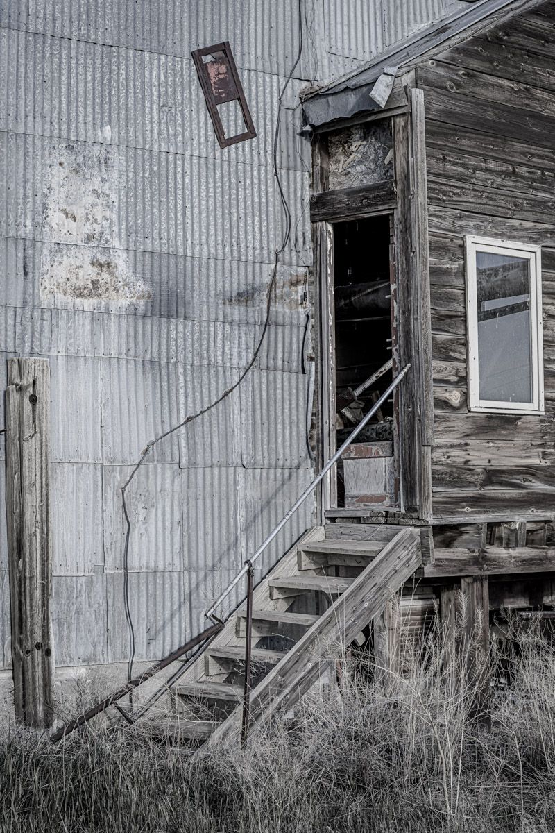 Weathered wooden staircase leads to entrance of abandoned building with metal siding.