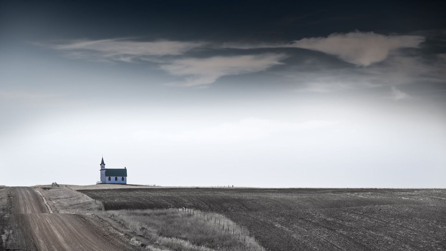 Solitary white church stands isolated on vast prairie horizon under dramatic sky.