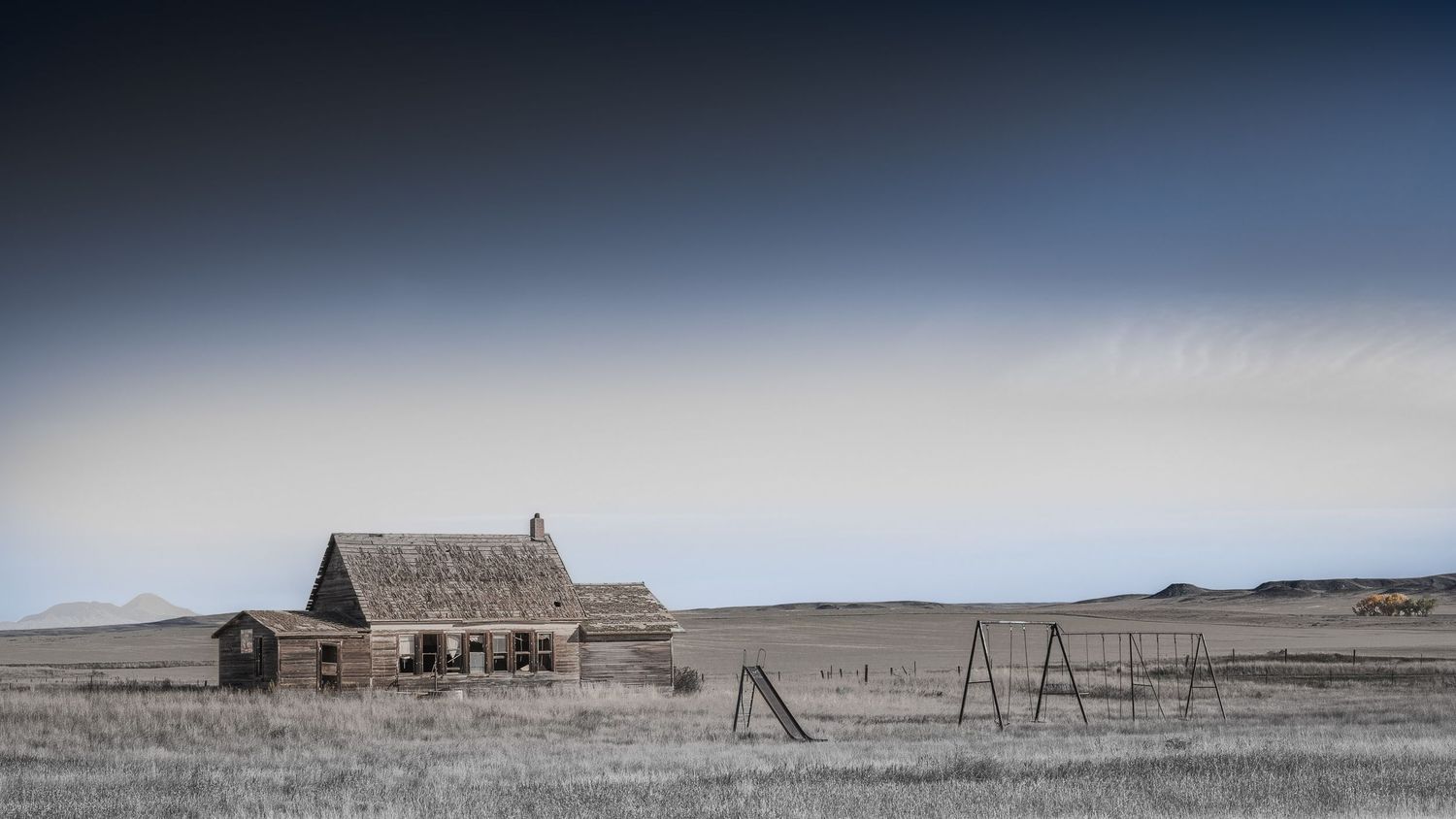 Old barn and playground equipment stand isolated in misty rural prairie landscape.