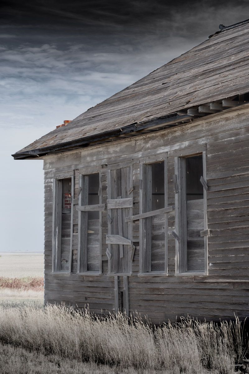 Weathered wooden house with broken windows and peeling paint stands isolated against a moody sky.