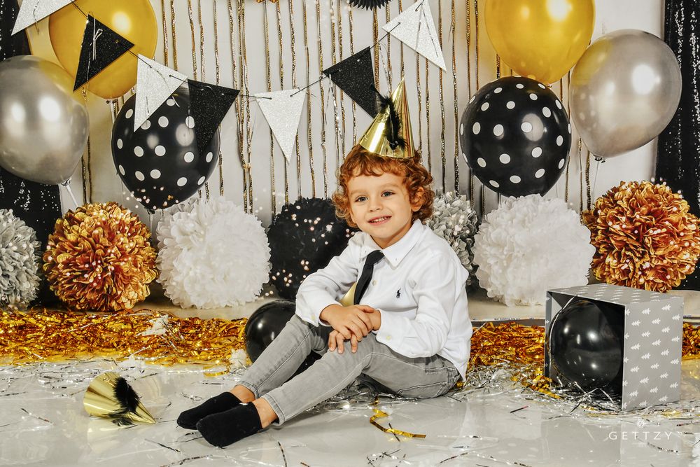 A festive birthday party setup with black and gold polka dot balloons, streamers, and glittery decorations against white backdrop.