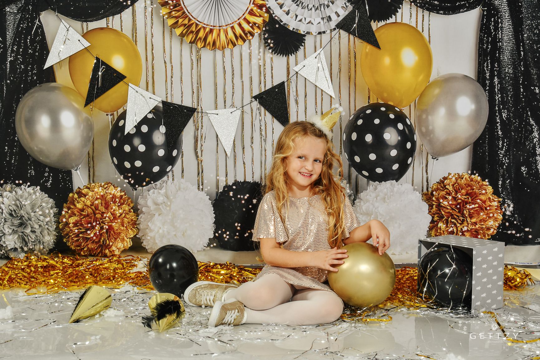 A festive new year party setup with polka dot balloons, gold accents, and silver decorations against a sparkly backdrop.