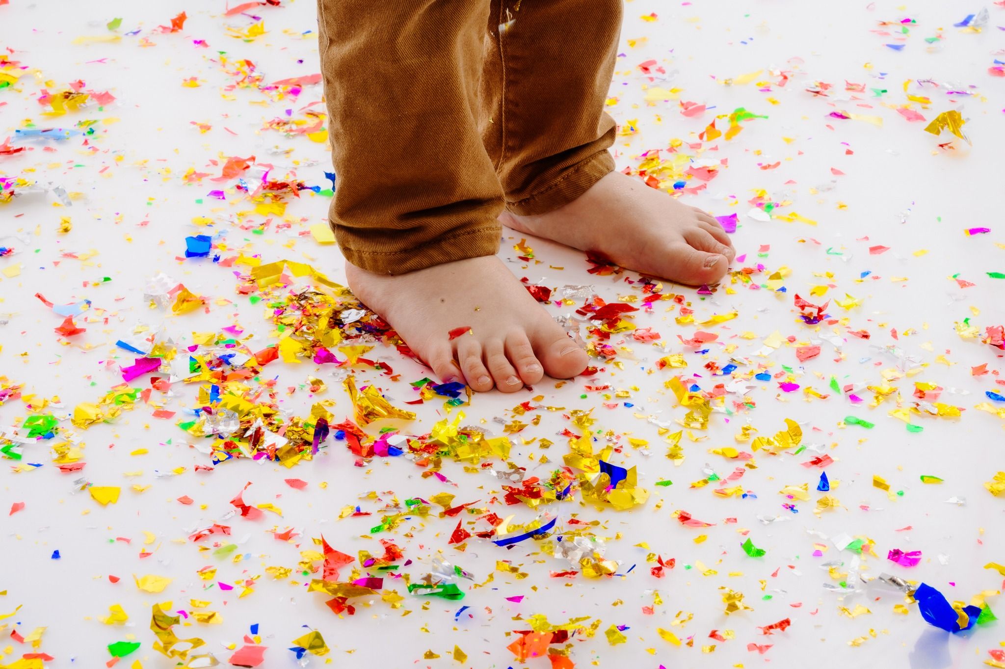 Bare feet standing on a white surface covered in colorful paint confetti and splashes.