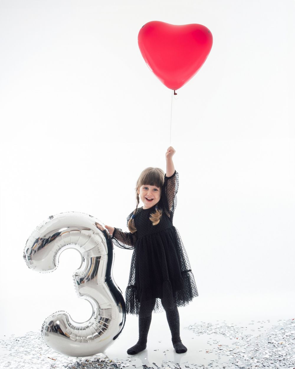 A silver number 3 balloon and red heart balloon decorate a minimalist celebration scene on white background.