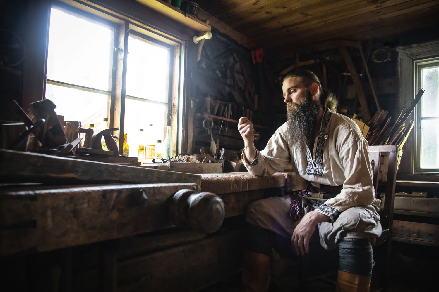 Craftsman works by window light in rustic workshop with traditional tools and wooden surroundings.