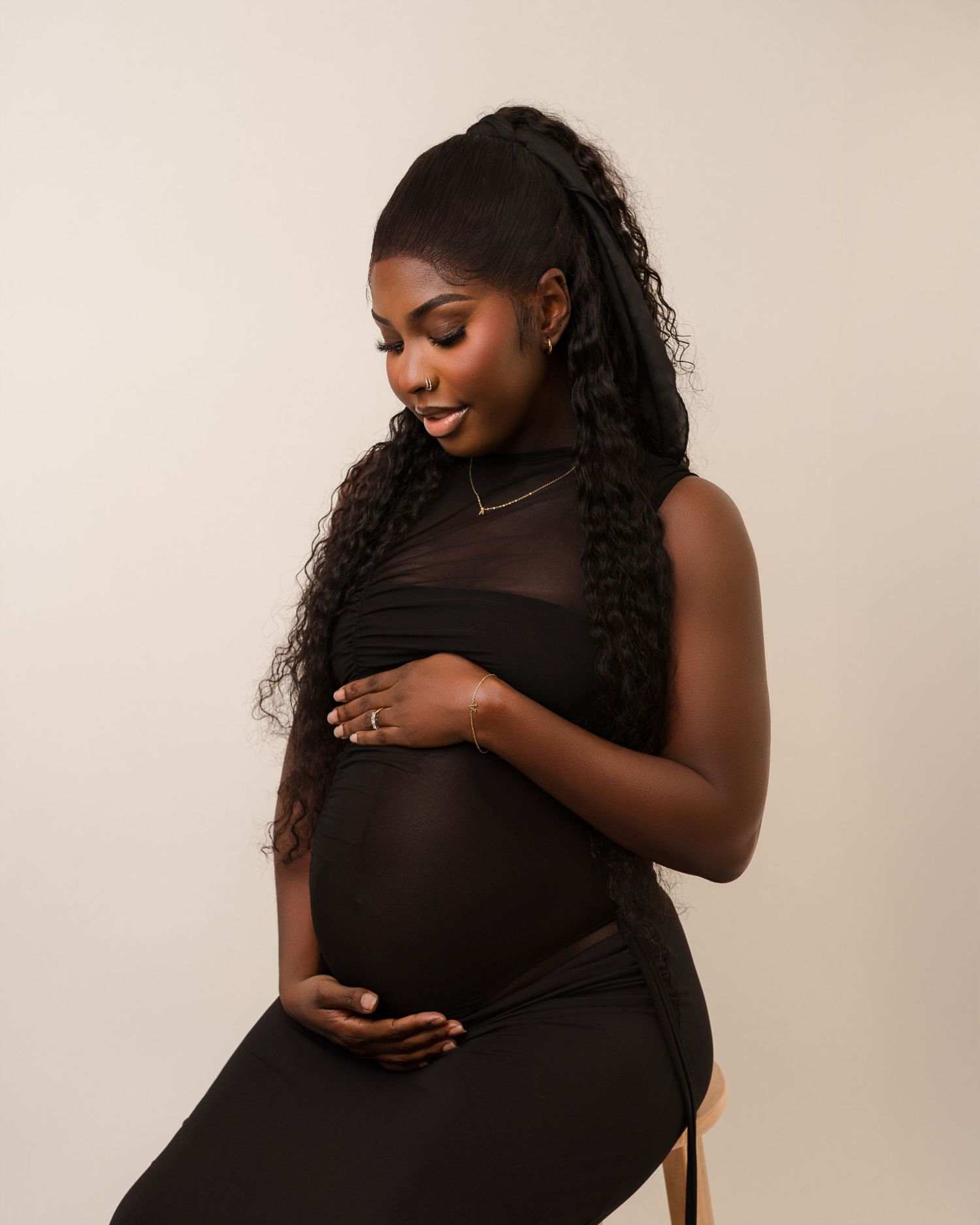 Silhouetted side profile maternity photo shoot showing pregnant woman in black outfit against neutral beige background.