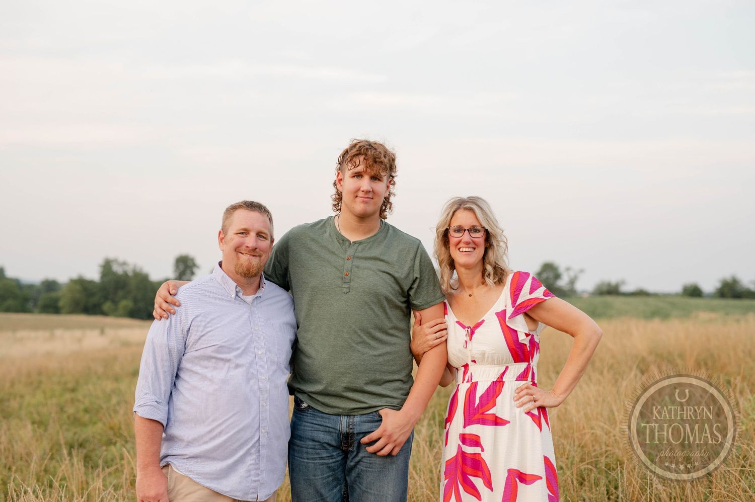 Three people stand together in a field during sunset with mountains in the background.
