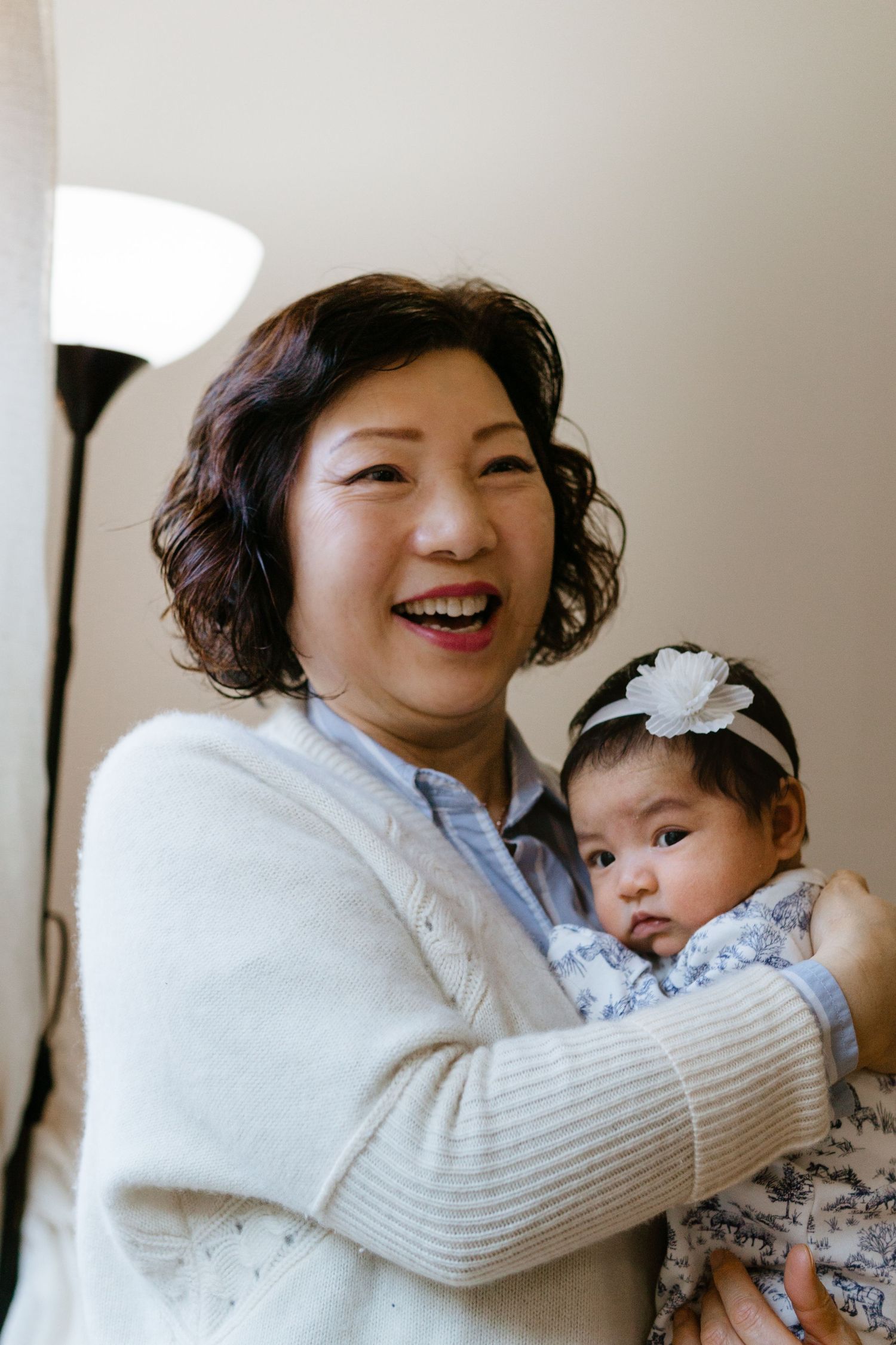 A heartwarming moment shows grandma holding a small baby wearing a floral dress and white headband.