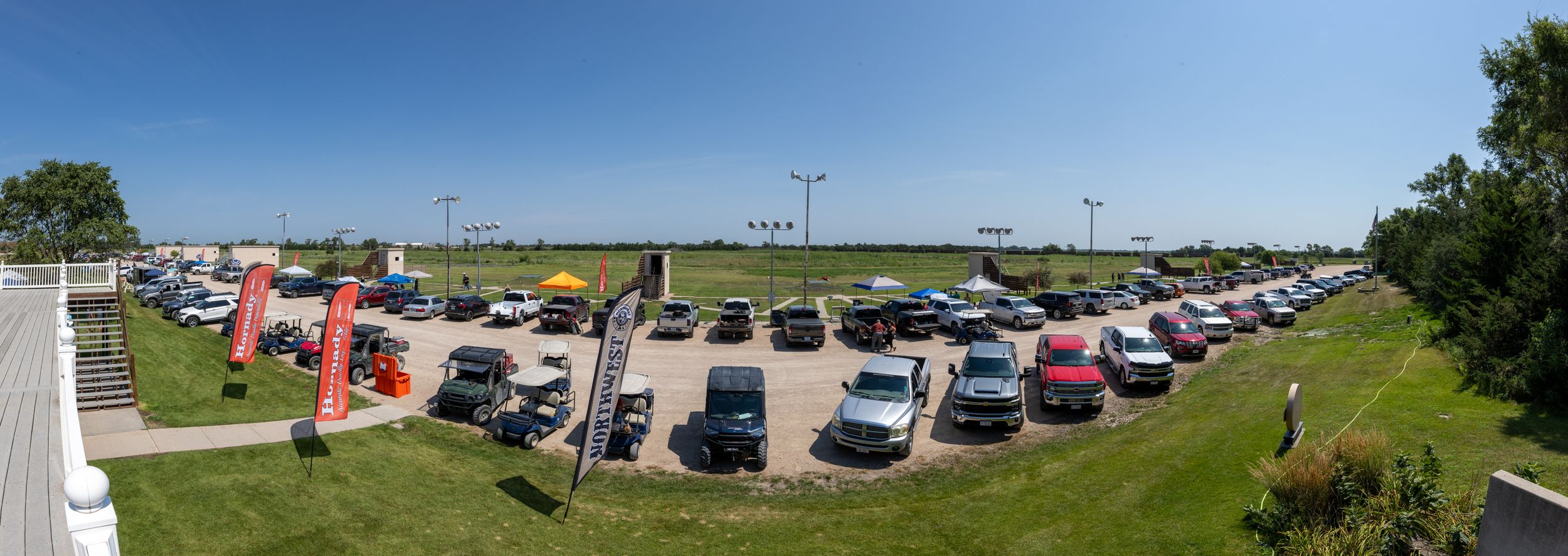 Wide panorama of a busy parking lot surrounded by green trees and buildings.