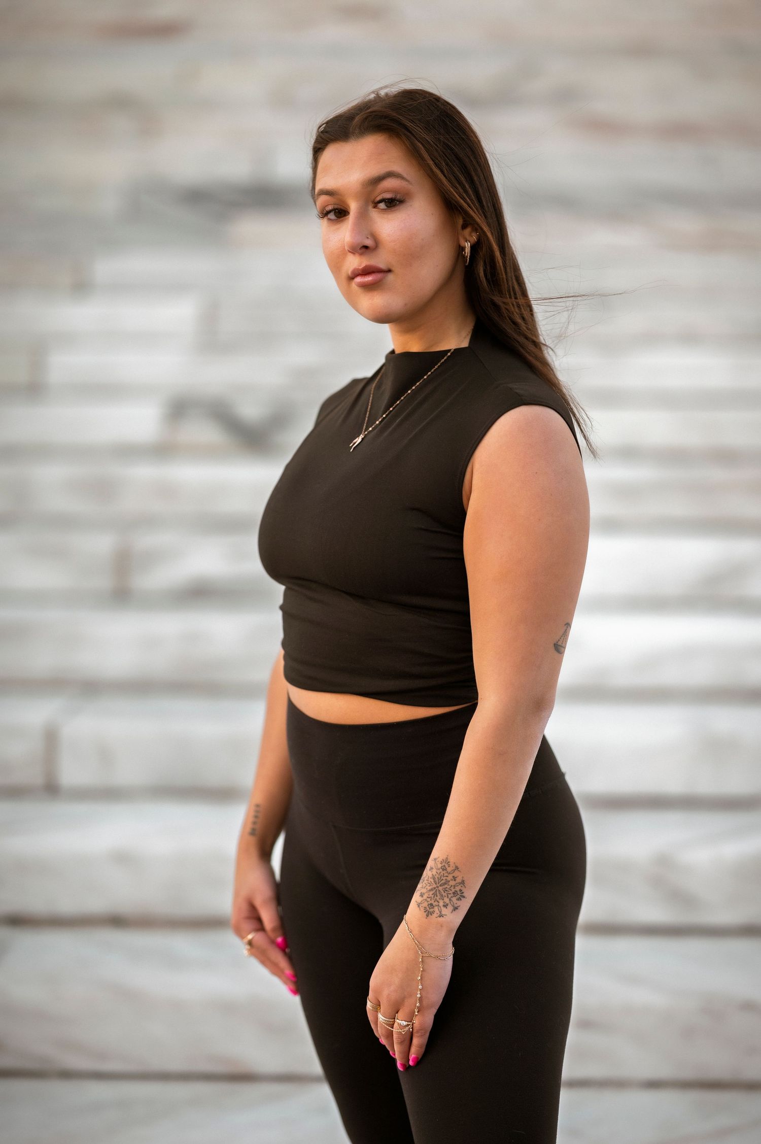 Athletic figure in a black crop top and matching leggings poses on stairs during an outdoor photoshoot.