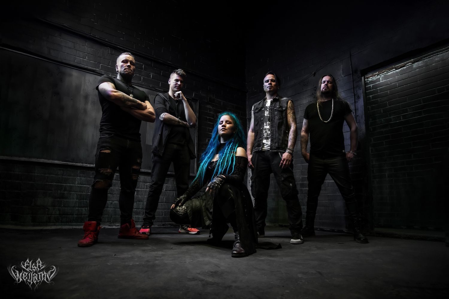 Hard rock band poses dramatically in dark industrial setting with dramatic low-angle lighting on black walls.