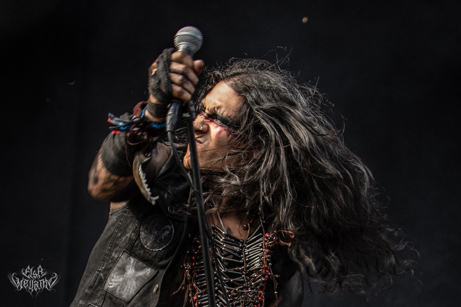 Dramatic low-angle shot of a rock musician with long dark hair performing passionately on stage with a microphone.