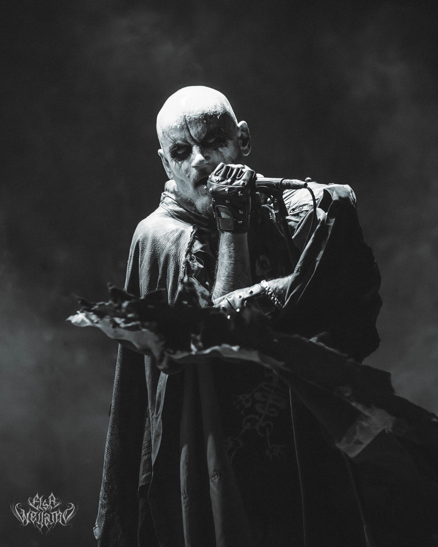 Dramatic black and white photo of a mysterious figure in dark robes holding a camera in atmospheric smoke.