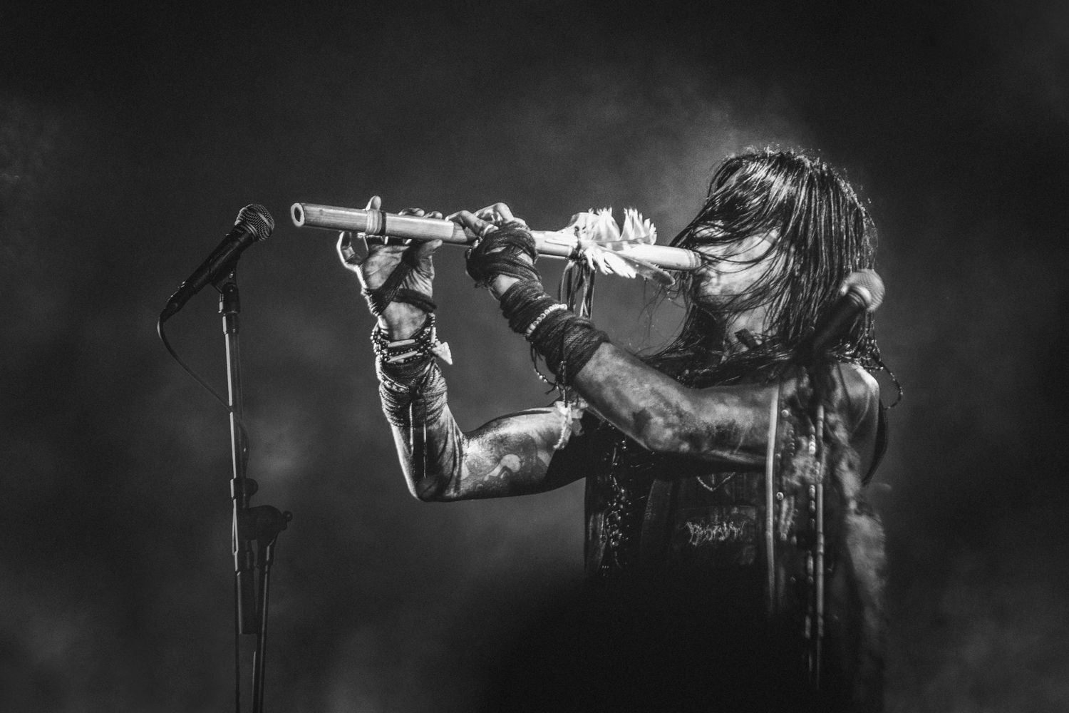 Dramatic black and white concert photo of a performer playing a wind instrument on stage with dramatic lighting.