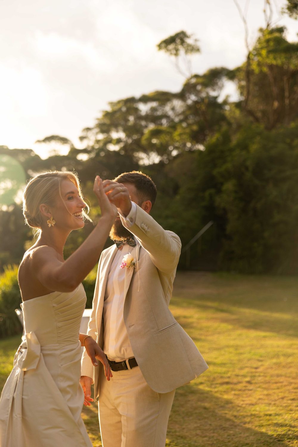A couple in wedding attire dances together in a grassy field at sunset, creating a romantic silhouette.