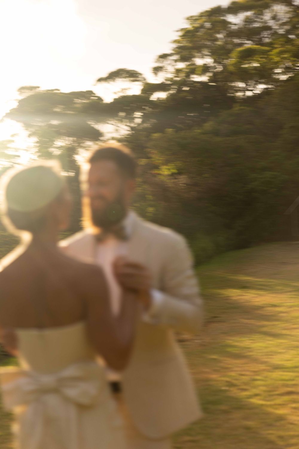 A couple dances together at sunset in a garden setting with soft golden light and trees in the background.