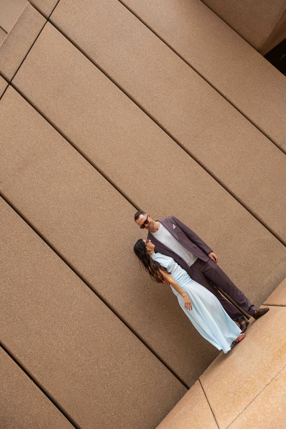 Two people in formal attire stand together on beige stone steps for a photo shoot.
