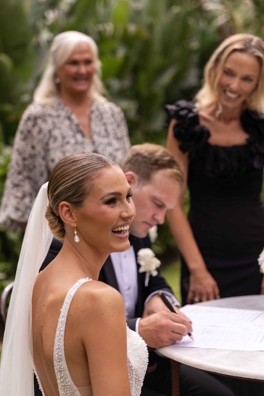 A series of candid wedding ceremony moments showing a bride signing documents with guests and family members.